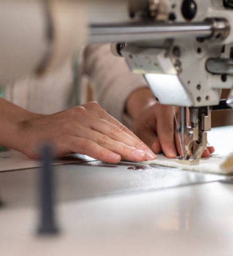 In front of the camera good looking dressmaker using her professional sewing machine to sew a dress closeup taking video details.