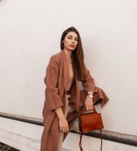 Stylish beautiful girl in fashionable outerwear stands near the wall