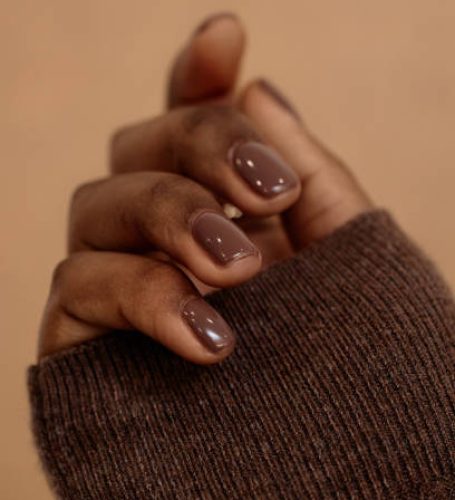 Vertical close up on manicure for fall nail inspiration in chocolate color on beige background. Warm brown nails of African American woman for autumn, copy space